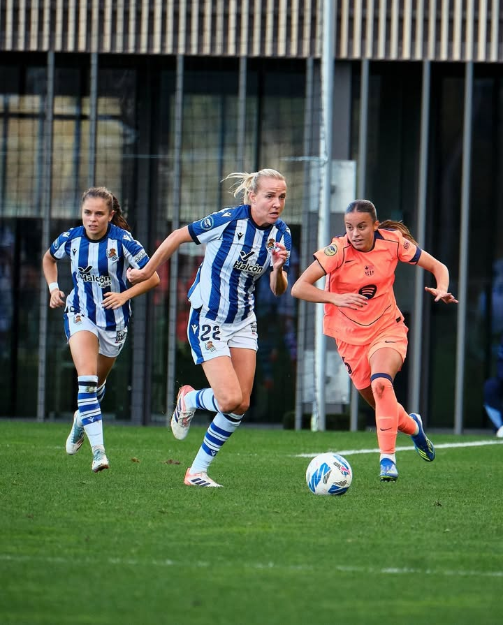 Clara Serrajordi persigue el balón ante la atenta mirada de dos jugadoras del conjunto vasco. Fuente: @realsociedadfem.