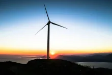Imagen de un aerogenerador en lo alto de una colina al borde de una ría