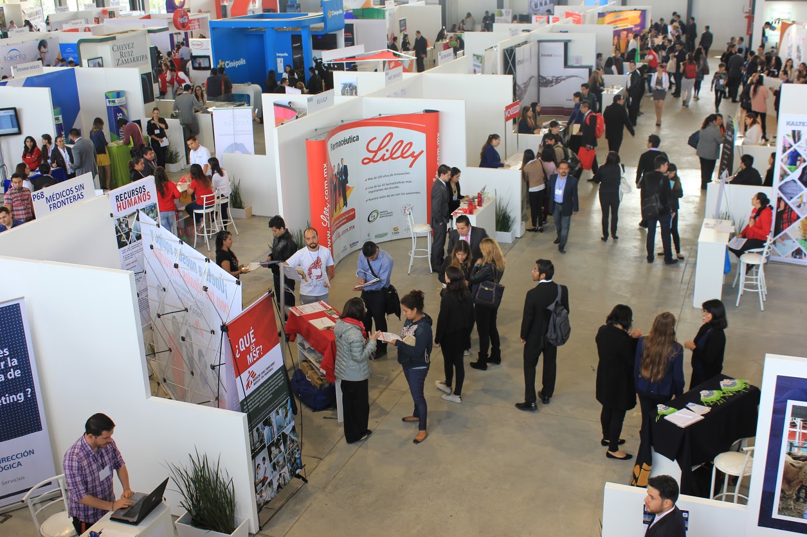 Fotografía de una feria de empleo en un pabellón, con múltiples stands informativos alineados y numerosos asistentes interactuando con los expositores. La imagen refleja un ambiente dinámico de networking y búsqueda de oportunidades laborales.